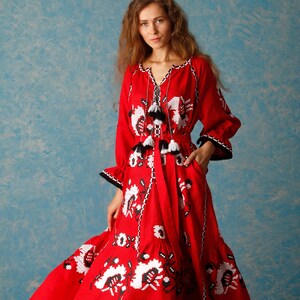 May include: A red linen dress with white and black embroidery. The dress has a long skirt and a fitted bodice. The dress is decorated with tassels. The dress is shown on a model against a blue background. etsy.com/shop/HelenCloth