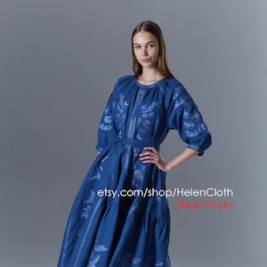 May include: A blue linen dress with embroidered floral designs. The dress has a cinched waist with a matching fabric belt and a tiered skirt.