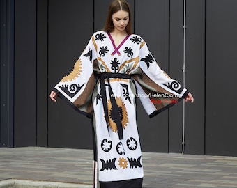 May include: A white, black, and brown long-sleeved dress with a geometric pattern and a black belt. The dress has a V-neckline and a long, flowing skirt.