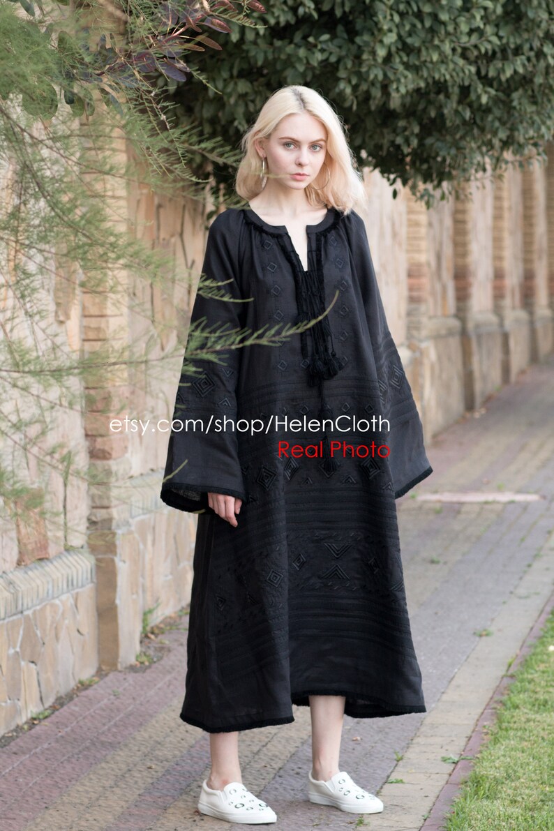 May include: A black embroidered linen dress with long sleeves and a round neckline. The dress has a geometric pattern and a tassel detail at the neckline. The model is wearing white sneakers. etsy.com/shop/HelenCloth Real Photo