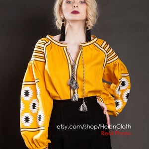 May include: A yellow embroidered blouse with black and white geometric patterns and long sleeves. The blouse has a V-neckline and a tie at the neckline. The model is wearing a black skirt. The text "etsy.com/shop/HelenCloth Real Photo" is visible at the bottom of the image.
