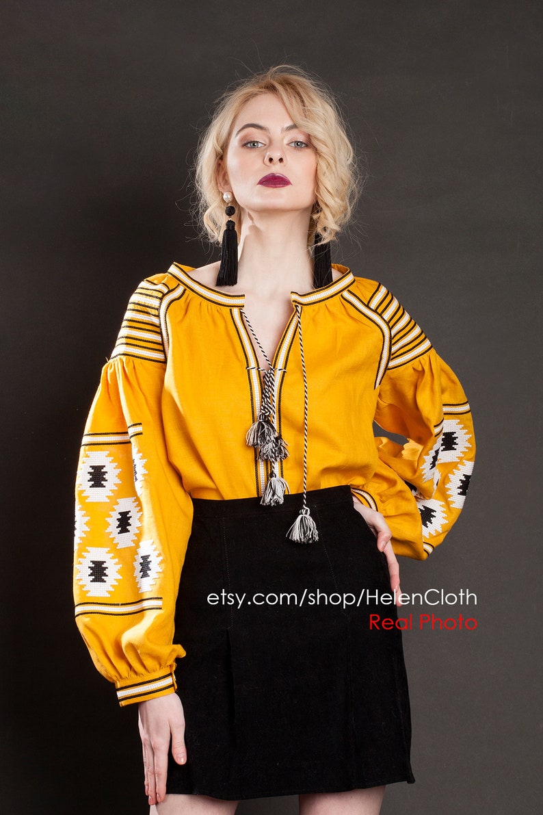 May include: A yellow embroidered blouse with black and white geometric patterns and long sleeves. The blouse has a V-neckline and a tie at the neckline. The model is wearing a black skirt. The text "etsy.com/shop/HelenCloth Real Photo" is visible at the bottom of the image.