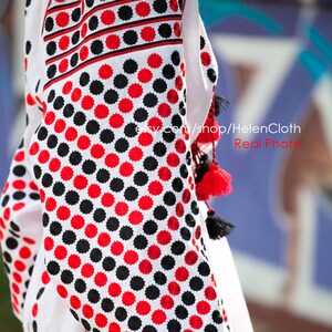 May include: White linen blouse with red and black embroidered polka dots. The embroidery is a traditional Ukrainian design. The blouse has long sleeves and a round neckline.