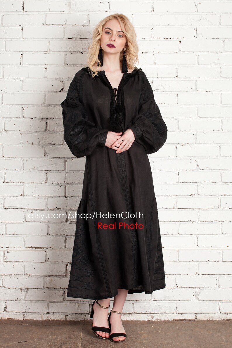 Pu&ograve; includere: Un abito in lino nero con maniche lunghe e scollo arricciato. L'abito ha un laccio al collo e un dettaglio a nappina. La modella indossa l'abito con sandali neri con tacco. Il testo "etsy.com/shop/HelenCloth Real Photo" &egrave; visibile nella parte inferiore dell'immagine.