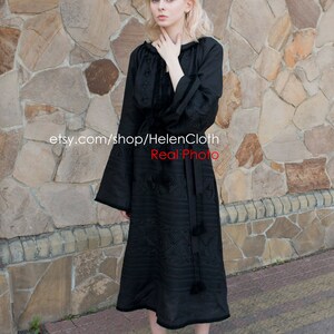 May include: A black embroidered dress with long sleeves and a gathered neckline. The dress has a geometric pattern and is worn by a person standing in front of a stone wall. The text "etsy.com/shop/HelenCloth Real Photo" is visible on the dress.