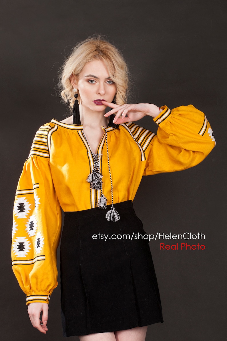 May include: A yellow embroidered blouse with black and white geometric patterns. The blouse has long sleeves and a round neckline. The model is wearing a black skirt and has long blonde hair. The text "etsy.com/shop/HelenCloth Real Photo" is visible at the bottom of the image.