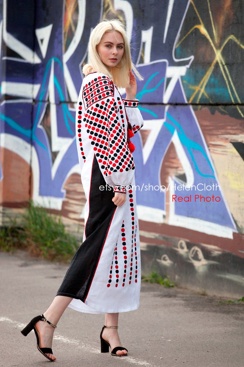 May include: A white linen dress with red and black polka dots embroidery. The dress has a long sleeve and a loose fit. The model is wearing black heeled sandals. The dress is photographed in front of a graffiti wall. The text "etsy.com/shop/HelenCloth Real Photo" is visible in the image.