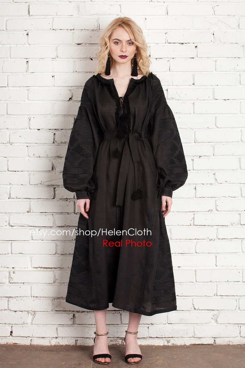 Pu&ograve; includere: Un abito in lino nero con maniche lunghe e ricami. L'abito ha una cintura e dettagli con frange. La modella indossa sandali neri e orecchini. Il testo "etsy.com/shop/HelenCloth Real Photo" &egrave; in basso nell'immagine.