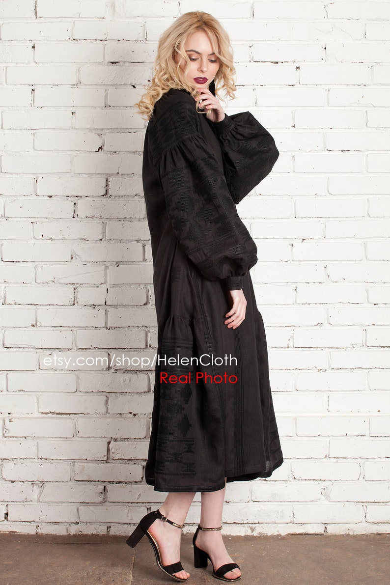 Pu&ograve; includere: Abito in lino nero ricamato con maniche lunghe e gonna a pieghe. L'abito &egrave; mostrato su una modella contro un muro di mattoni bianchi. Il testo "etsy.com/shop/HelenCloth Real Photo" &egrave; visibile nella parte inferiore dell'immagine.