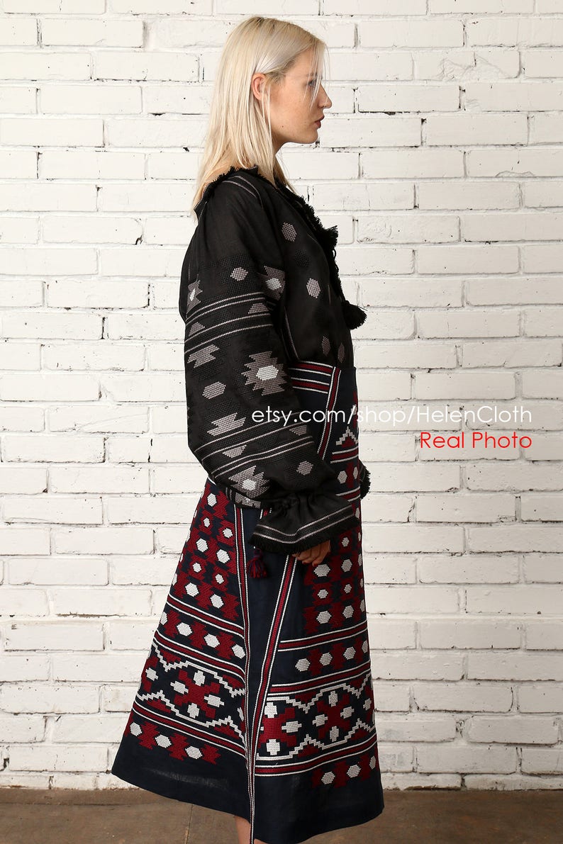 May include: A black and white embroidered blouse with long sleeves and a red and white embroidered skirt. The skirt has a geometric pattern. The model is standing in front of a white brick wall. etsy.com/shop/HelenCloth Real Photo