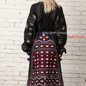 May include: A black linen blouse with embroidered geometric patterns and a long, dark blue skirt with red and white embroidered geometric patterns. The skirt has tassels on the bottom.