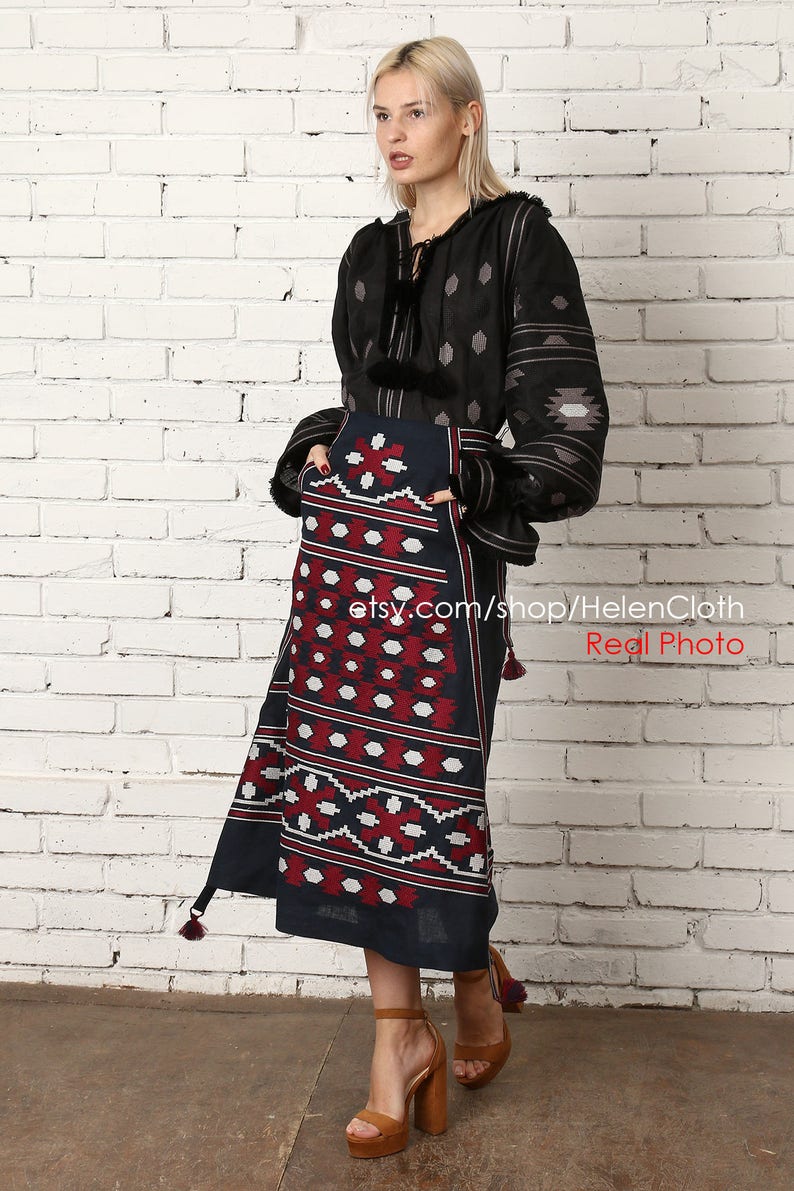 May include: A black and gray embroidered linen blouse with a long sleeve and a geometric pattern. The blouse is paired with a blue and red patterned skirt with a geometric design. The skirt has a tassel detail at the bottom. The model is wearing brown high-heeled sandals. etsy.com/shop/HelenCloth Real Photo