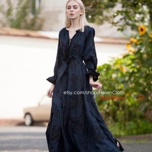 May include: A woman wearing a dark blue maxi dress with black embroidery. The dress has a V-neckline and long sleeves. The woman is standing on a sidewalk and looking at the camera. The text "etsy.com/shop/HelenCloth Real Photo" is visible in the image.