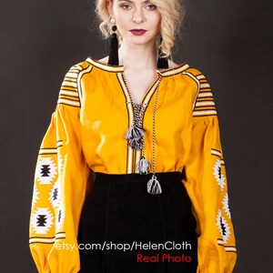 May include: A yellow embroidered blouse with black and white geometric patterns. The blouse has long sleeves and a V-neckline. The model is wearing a black skirt. The text "etsy.com/shop/HelenCloth Real Photo" is visible on the image.