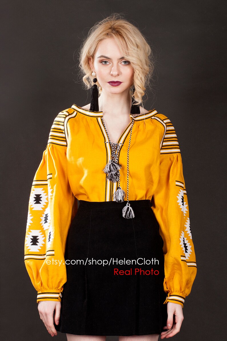 May include: A yellow embroidered blouse with black and white geometric patterns. The blouse has long sleeves and a V-neckline. The model is wearing a black skirt. The text "etsy.com/shop/HelenCloth Real Photo" is visible on the image.