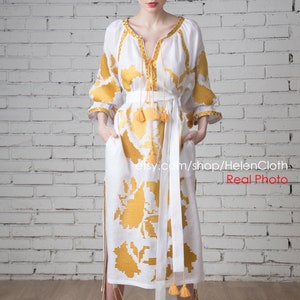 May include: A white linen dress with yellow embroidered floral patterns and tassels. The dress has a V-neckline and a long skirt. The model is wearing white sandals.  etsy.com/shop/HelenCloth Real Photo