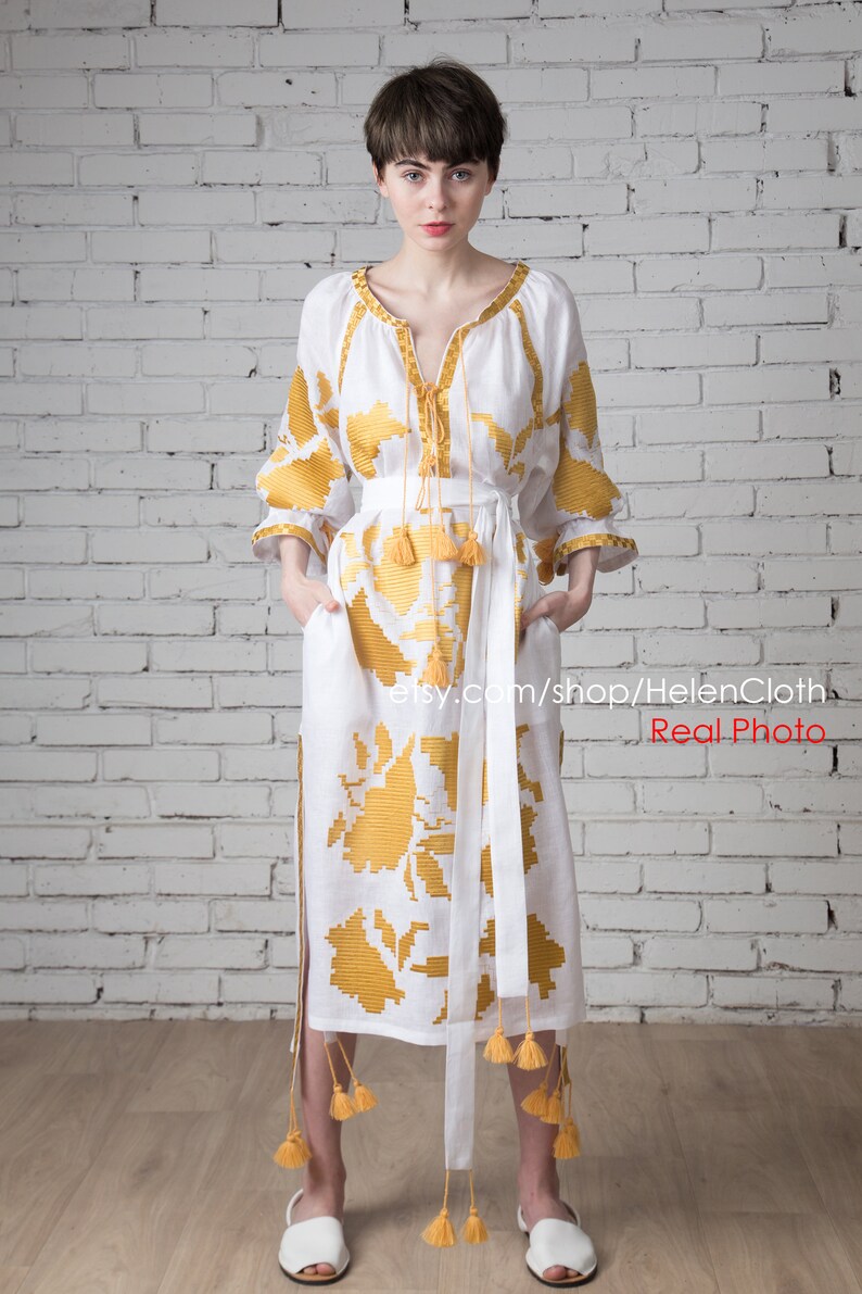 May include: A white linen dress with yellow embroidered floral patterns and tassels. The dress has a V-neckline and a long skirt. The model is wearing white sandals.  etsy.com/shop/HelenCloth Real Photo