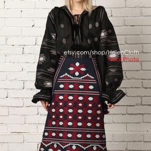 May include: A black embroidered blouse with long sleeves and a geometric pattern. The blouse is paired with a dark blue skirt with a red and white geometric pattern. The skirt is knee-length and has a tassel at the bottom. The model is wearing the outfit against a white brick wall. etsy.com/shop/HelenCloth Real Photo