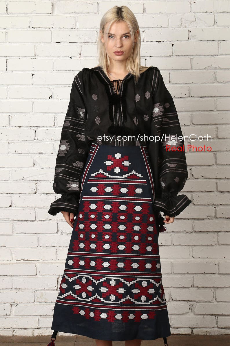May include: A black embroidered blouse with long sleeves and a geometric pattern. The blouse is paired with a dark blue skirt with a red and white geometric pattern. The skirt is knee-length and has a tassel at the bottom. The model is wearing the outfit against a white brick wall. etsy.com/shop/HelenCloth Real Photo