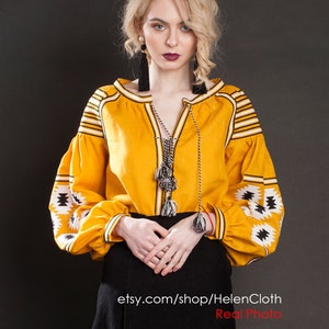 May include: A yellow embroidered linen blouse with black and white geometric patterns. The blouse has a V-neckline and long sleeves with a tassel detail. The model is wearing a black skirt and has blonde hair. The text "etsy.com/shop/HelenCloth Real Photo" is visible at the bottom of the image.