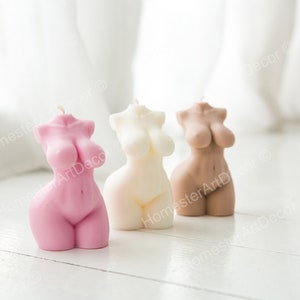 May include: Three decorative candles shaped like human figures. The candles are in pink, white, and brown.