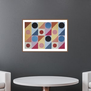 Könnte beinhalten: Ein gerahmter Kunstdruck mit einem geometrischen Muster aus farbigen Formen, darunter Kreise, Dreiecke und Quadrate. Das Kunstwerk hängt an einer dunkelgrauen Wand über zwei weißen Sesseln und einem runden Tisch und schafft ein modernes Innendesign.