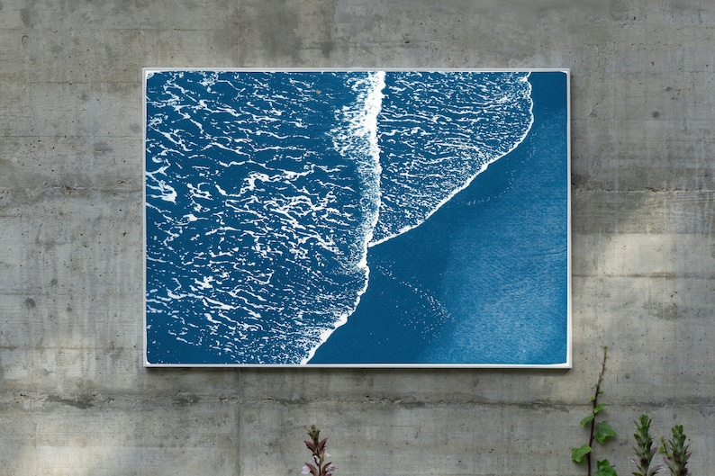 Puede incluir: Una impresi&oacute;n enmarcada de una imagen abstracta azul y blanca de olas del oc&eacute;ano rompiendo en una playa. La imagen est&aacute; enmarcada en un marco blanco delgado.