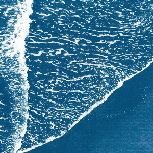 Puede incluir: Una vista a&eacute;rea abstracta de una ola rompiendo en una playa. El agua es de un color azul profundo y la ola es blanca con una cresta espumosa. La imagen recuerda a una pintura de acuarela azul y blanca.