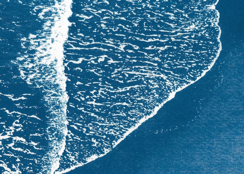 Puede incluir: Una vista a&eacute;rea abstracta de una ola rompiendo en una playa. El agua es de un color azul profundo y la ola es blanca con una cresta espumosa. La imagen recuerda a una pintura de acuarela azul y blanca.
