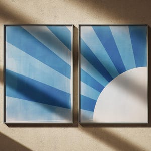 Puede incluir: Dos láminas de arte mural rectangulares en marcos finos. La lámina de la izquierda presenta rayas diagonales azules y azul claro. La lámina de la derecha muestra un semicírculo blanco en la esquina inferior derecha con rayos azules.