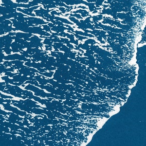 Puede incluir: Primer plano de una ola rompiendo en la costa, creando una cresta blanca espumosa sobre un fondo de oc&eacute;ano azul profundo.
