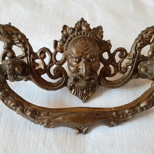 Può includere: Una maniglia per porta in ottone vintage con un design decorativo che presenta un viso grottesco e volute ornate.