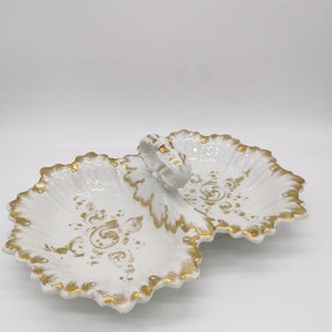 Puede incluir: Un plato de servir de porcelana blanca con dos secciones y un asa dorada. El plato está decorado con un patrón floral dorado.