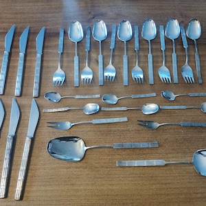 Könnte beinhalten: Eine Sammlung von Edelstahlbesteck, darunter Messer, Gabeln, Löffel und Servierlöffel, angeordnet auf einer Holzoberfläche. Das Besteck hat ein strukturiertes Griffdesign.
