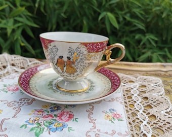 Footed courting couple, romantic scenes tea cup and saucer, red and gold lustre cup