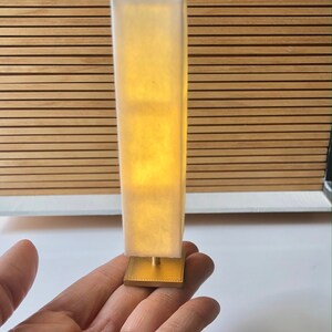 Op de afbeelding: Een witte lamp met een gouden voet. De lamp is aan en geeft een warm licht.
