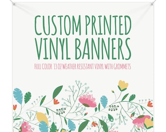 May include: White vinyl banner with green text that reads "CUSTOM PRINTED VINYL BANNERS" and "FULL COLOR 13 OZ WEATHER RESISTANT VINYL WITH GROMMETS". The banner has a floral border with pink, yellow, and blue flowers.