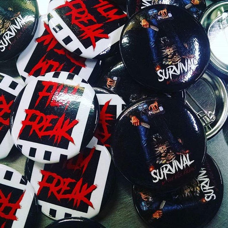 May include: A collection of round, black and white buttons with various designs. Some buttons feature the text "Film Freak" in red lettering, while others feature the text "Survival" in white lettering.