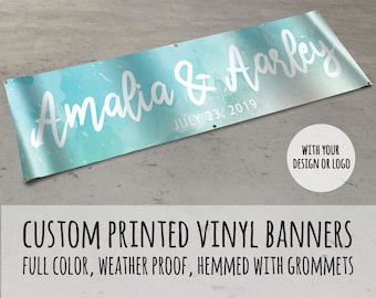 May include: A custom printed vinyl banner with a watercolor background in shades of blue and green. The banner reads "Amalia & Aarley" in white script font with the date "July 23, 2019" below. The banner is hemmed with grommets and is weatherproof.