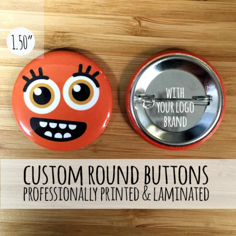 May include: Two 1.5 inch round custom buttons. One button features a cartoon face with orange skin, black eyes, and a wide smile. The other button is blank with the text "WITH YOUR LOGO BRAND".