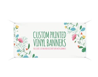 May include: White vinyl banner with green text that reads "CUSTOM PRINTED VINYL BANNERS" and "FULL COLOR, 13 OZ WEATHER RESISTANT VINYL WITH GROMMETS". The banner has a floral design with pink, yellow, and blue flowers.