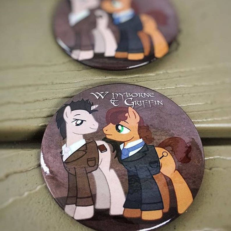 May include: Two cartoon ponies wearing suits. The pony on the left is gray and the pony on the right is brown. The text "Wyborne & Griffin" is printed on the button.