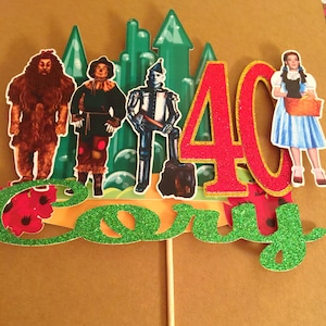 May include: A green and red cake topper with the number 40, the word "Cory", and characters from the Wizard of Oz. The characters include the Tin Man, the Scarecrow, the Cowardly Lion, and Dorothy.