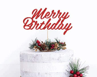 May include: A red glitter "Merry Birthday" cake topper on a white frosted cake. The topper is on a wooden stick and is surrounded by pine needles, berries, and pinecones. The cake has a rustic, textured appearance.