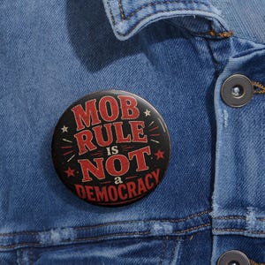 May include: A round black button with the text "MOB RULE IS NOT a DEMOCRACY" in red and white. The button is pinned to a blue denim jacket.