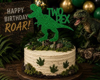 May include: A round cake with light-colored frosting, decorated with green dinosaur footprint cutouts and mossy textures. A green glittery cake topper shaped like a Tyrannosaurus Rex features the text TWO REX, supported by two wooden sticks.