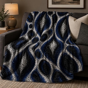 May include: A navy blue, black, and silver throw blanket with an abstract pattern draped over a gray sofa. The design features interconnected oval and circular shapes. The blanket is made of a soft, textured material, perfect for adding warmth and style to any living space.