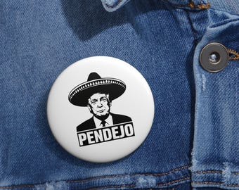 May include: A white button with a black and white image of a person wearing a sombrero and the word "PENDEJO" printed below.