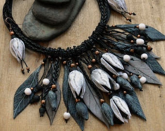 May include: A black leather necklace with a fringe of white and grey polymer clay flowers and leaves. The necklace is handmade by AlekSanta.