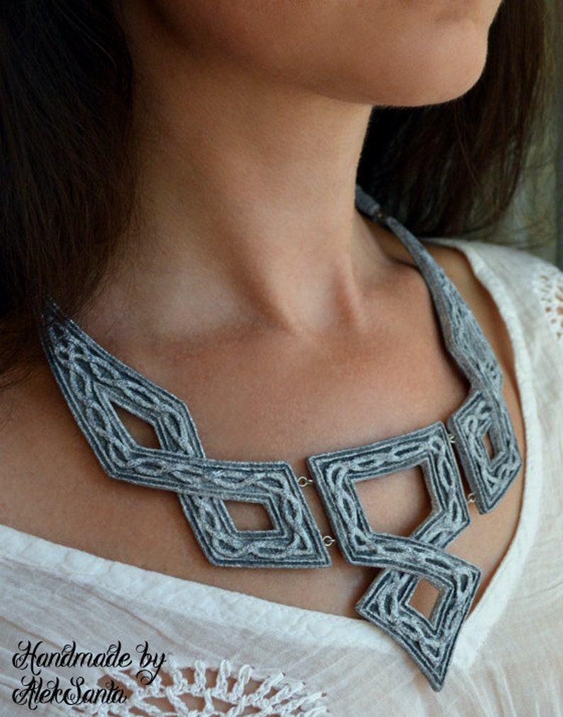 Puede incluir: Un collar de fieltro gris con un dise&ntilde;o geom&eacute;trico. El collar est&aacute; hecho de m&uacute;ltiples hebras de fieltro que se tejen juntas para crear un patr&oacute;n &uacute;nico e intrincado. El collar es una pieza llamativa que a&ntilde;adir&iacute;a un toque de elegancia a cualquier atuendo.